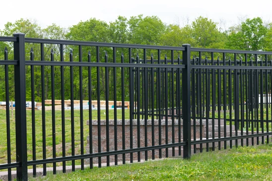 Portail résidentiel en fer forgé noir avec ornements décoratifs, piliers en briques beiges, clôture assortie